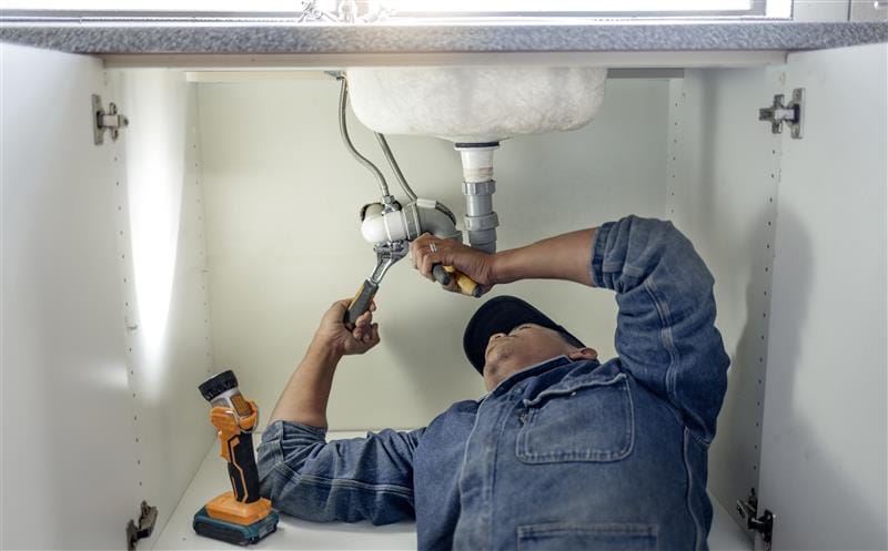 Plumber repairing pipes beneath a bathroom sink in Cheltenham