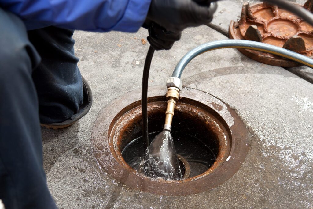 Plumber hydro jetting a sewer line through a manhole in Cheltenham