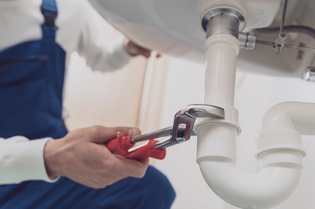 Plumber repairing a white drain pipe beneath a sink in Cheltenham