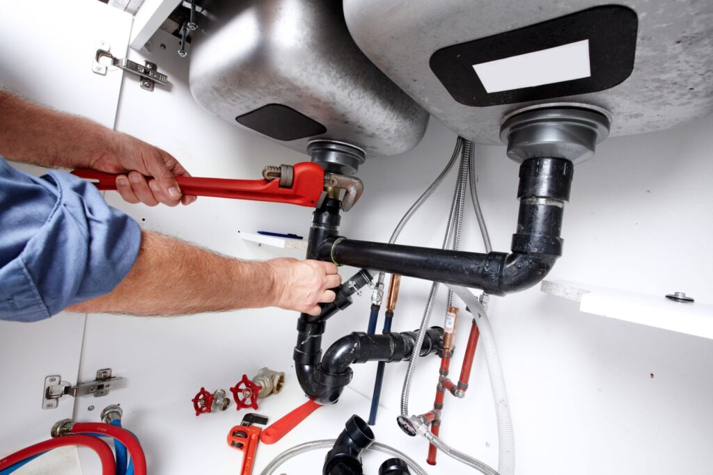 Plumber repairing drain pipes beneath a kitchen sink in Cheltenham